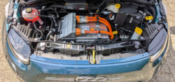 Der Motorraum eines Fiat 500e. Unter der geöffneten Motorhaube sieht man dicke orange Stromkabel und verschiedene andere Aggregate.