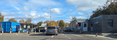 Einfahrt zu einem Recyclinghof der Stadtwerke. Einige Autos stehen in einer Schlange und warten. Man sieht Container für Elektrogeräte und ein Verwaltungsgebäude.