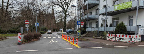 Die Einfahrt einer für den Radverkehr in Gegenrichtung freigegebenen Einbahnstraße mit einem rechts markierten Fahrstreifen für Fahrräder, welcher mit kleinen Kunststoffpollern von der Fahrbahn für Kfz abgetrennt ist.