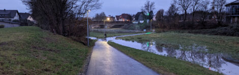 Ein Radfahrer quert eine Wasserfläche auf einem in einer Mulde gelegenen Geh- und Radweg.