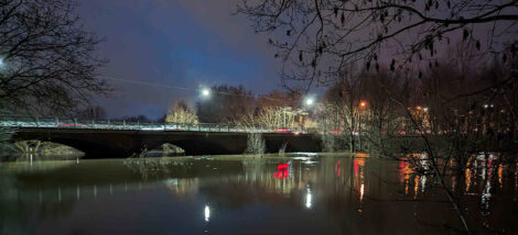 Eine Brücke über einen Fluss bei Nacht. Die Lichter der Straßenlaternen und Autos spiegeln sich auf der Wasseroberfläche.