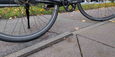 Eine hochstehende Kante auf der Grenze zwischen einem apshaltierten Radweg und dem aus Platten bestehenden Gehweg.