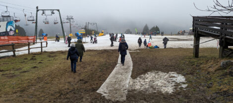 Eine Skigebiet bei dem nur noch die Piste mit Schnee bedeckt ist. Der Weg dorthin geht über braunes Gras.