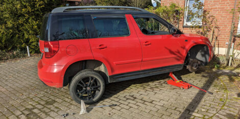 Ein rotes Auto - Skoda Yeti - ist vorne rechts auf einem Wagenheber und das rechte Vorderrad ist demontiert.