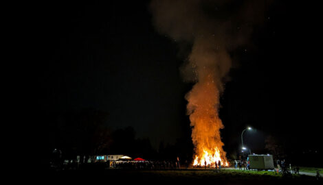 Ein Osterfeuer mit einer hohen Rauchsäule und im Verhältnis sehr kleinen Gertränke- und Wurstbuden.