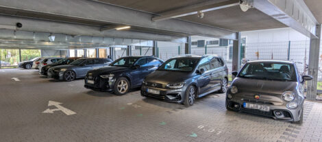 Etliche KFZ stehen in einem Parkhaus in einer Reihe.