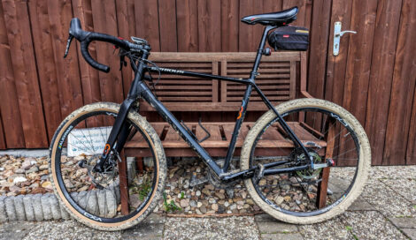 Ein schwarzes Gravelbike vor einem Holzschuppen mit verschlammten Reifen.