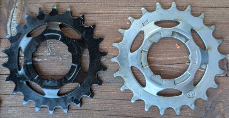 Ein schwarzes und ein silbernes Antriebsritzel von Shimano mit je 22 Zähnen. Das silberne ist sichtbar verschlissen