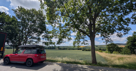 Ein roter Skoda Yeti steht auf einem Parkplatz vor einem Baum. Am strahlend blauen Himmel sind weiße, große Wolken zu sehen.