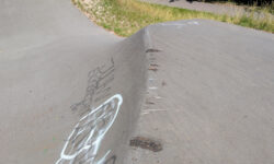 Man sieht die Kante einer asphaltierten Pumptrackanlage. Oben ist der Asphalt eben und dann geht er in steilem Winkel nach unten. Direkt an der Kante sind Kratzer und Abbrüche zu erkennen.