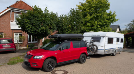Ein roter Skoda Yeti mit einem angekuppelten Wohnwagen vor einem Einfamilienhaus.