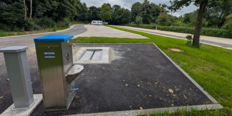 Ein großer, gesplitteter Wohmobilstellplatz, welcher u-förmig angelegt ist. Im Vordergrund sieht man die Entsorgungsanlage und Frischwasserversorgung. Ganz entfernt, am anderen Ende des Platzes, steht perspektivisch sehr klein, ein Wohnwagen.