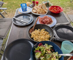 Ein gedeckter Campingtisch mit frischem Salat, Rührei und gebratenem Speck.