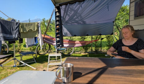 Ein Frau sitzt an einem Campingtisch unter der Markise vor einem Wohnwagen.