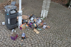 Auf einer gepflasterten Fläche liegt rund um einen Mülleimer allerlei Feuerwerksabfall.