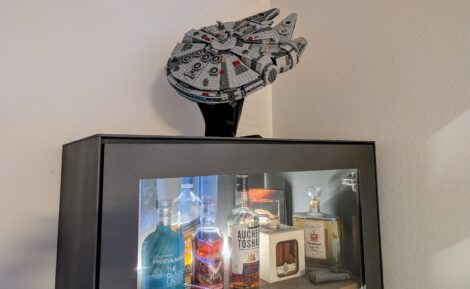 Ein Wohnzimmerschrank mit einer Glastür. Im beleuchteten Inneren des Schranks steht eine kleine Auswahl an Single-Malt-Whisky. Auf dem Schrank steht ein Millenium-Falcon aus Lego auf einem schwarzen Ständer mit der Front nach schräg oben.
