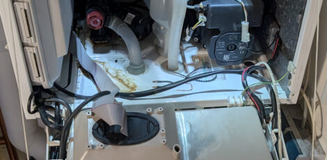 Das Innenleben einer Gastherme bei geöffneter Frontklappe. Man sieht Kabel, Schläuche und lose Kabelenden.