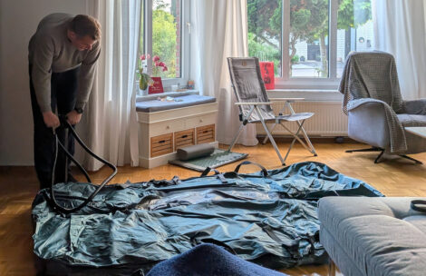 Ein Mann pumpt mit einer Standluftpumpe den Boden eines Zeltes in einem Wonzimmer auf.