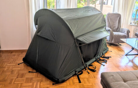 Ein grünes Dachzelt "Groenberg Weekend Comfort" steht aufgebaut in einem Wohnzimmer mit Parkettfußboden.