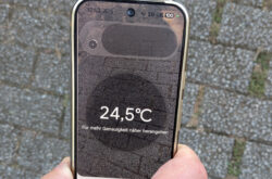 Das Thermometer eines Google Pixel 9 pro wird ca. 30 Zentimeter über im Baumschatten liegende Pflastersteine eines Weges gehalten und zeigt 24,5°C an.
