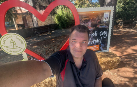 Ein Mann blickt leicht geschafft vor einem großen Herz als Fotospot in die Kamera und macht ein Selfie.