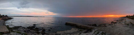 Panoramaaufnahme der Adria mit rotem Sonnenuntergang rechts im Bild, Gewitterwolken in der Mitte und blauem Himmel ganz links