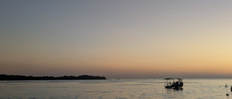 Die Venus ist als etwas hellerer Pixel ca. in der Mitte des Bildes über dem Meer zu erahnen. Leicht außermittig rechts im Bild ist ein Boot auf dem Meer.