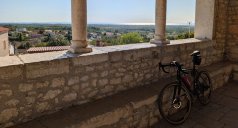 Blick aus einem Raum mit offener Fensterfront über eine bewaldete Landschaft bis zum Meer am Horizont.