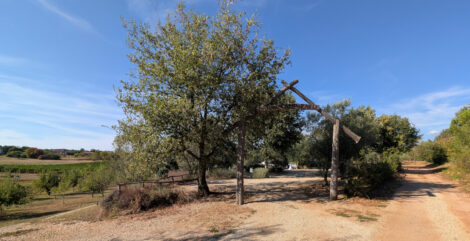 Der Eingang zu einem urigen Naturcampingplatz mit sehr wenigen Wohnwagenstellplätzen. Der Boden ist gesplittet und es stehen viele Bäume um die Parzellen.