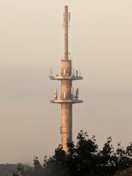 Ein Funkturm in der Morgensonne. Man sieht einzelne Antennen auf den kleinen Betonplattformen an der zentralen Säule.
